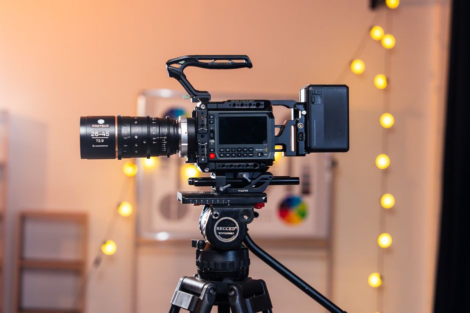 A high-quality video camera mounted on a tripod in a warmly lit studio setting with bokeh lights.
