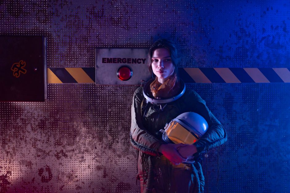 A futuristic woman astronaut standing near an emergency button in a sci-fi setting.