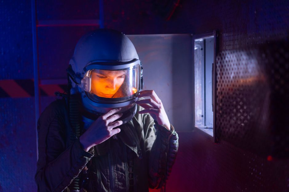 An astronaut in a spacesuit adjusts their helmet in a sci-fi setting.