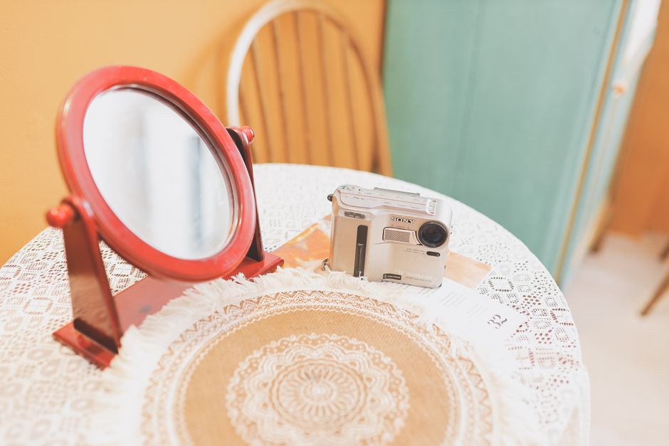 A retro setup with a vintage camera and a red mirror on a lace-covered table.