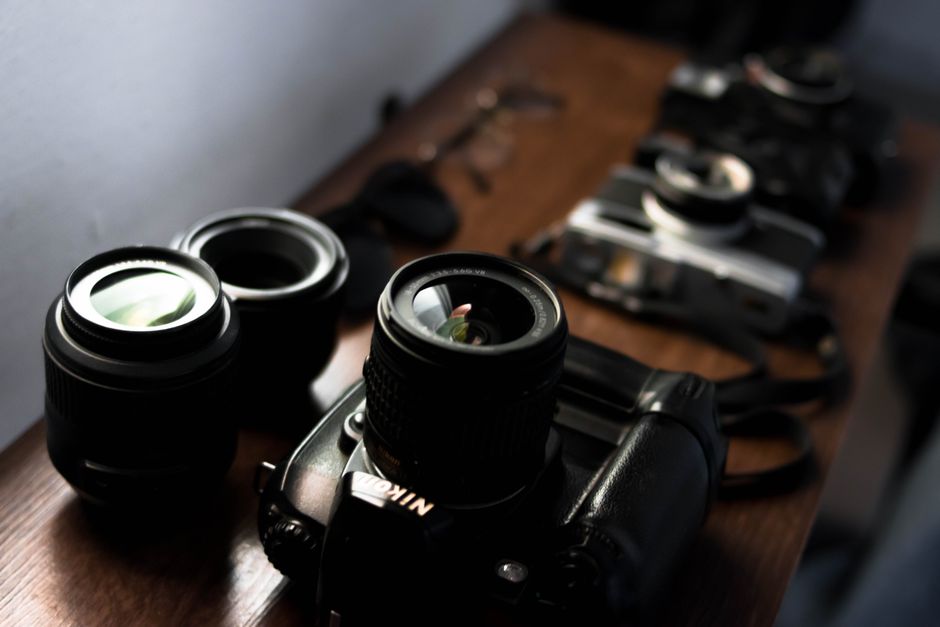 High angle collection of modern and retro photo cameras arranged on wooden table with professional lenses and sunglasses