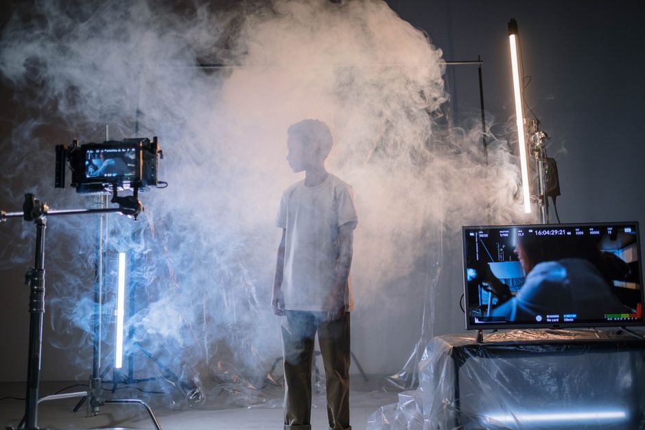A young boy stands amidst smoke in a high-tech studio, surrounded by screens and lighting.