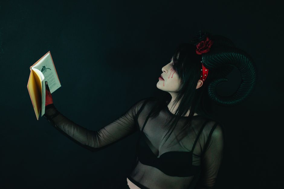 Artistic portrait of a woman in a horned costume holding a book, evoking a dark fantasy theme.