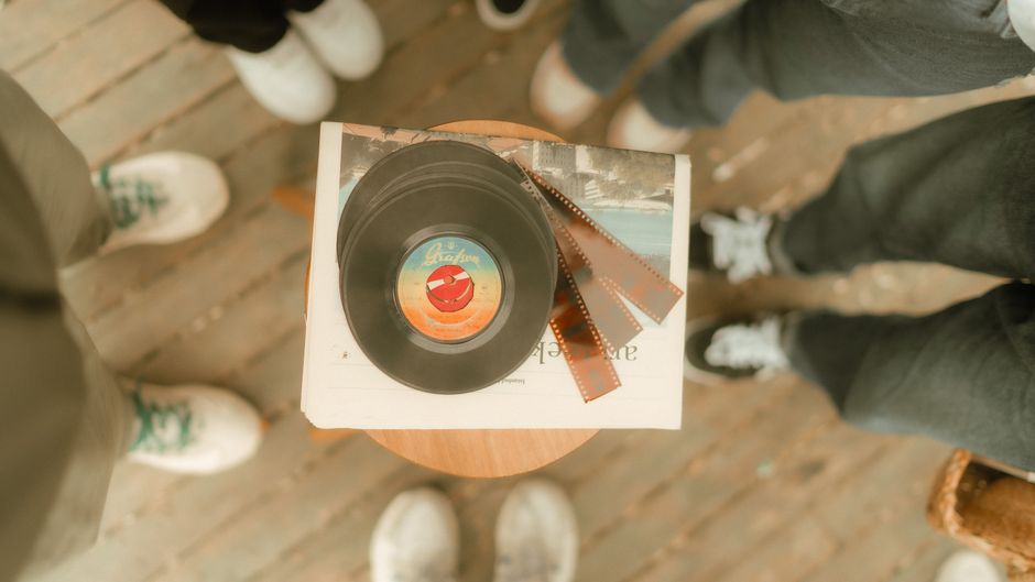 Overhead view of vinyl record and film strips surrounded by people on a wooden floor.
