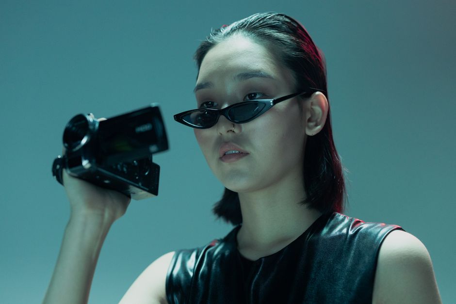 Portrait of a woman in cyberpunk style holding a camcorder with futuristic sunglasses.