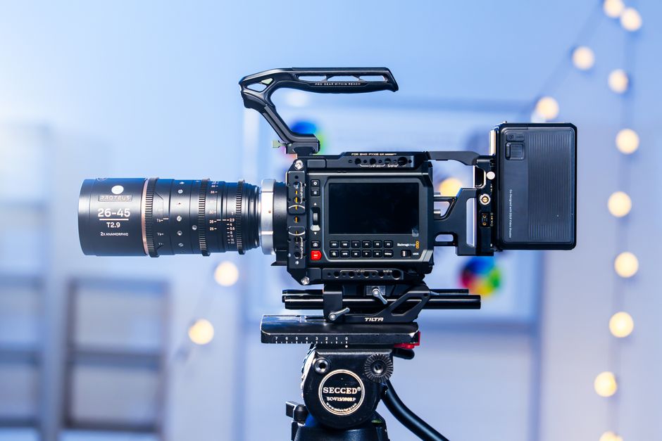 Side view of a professional video camera with a 26-45mm anamorphic lens on a tripod, indoors with bokeh lights.