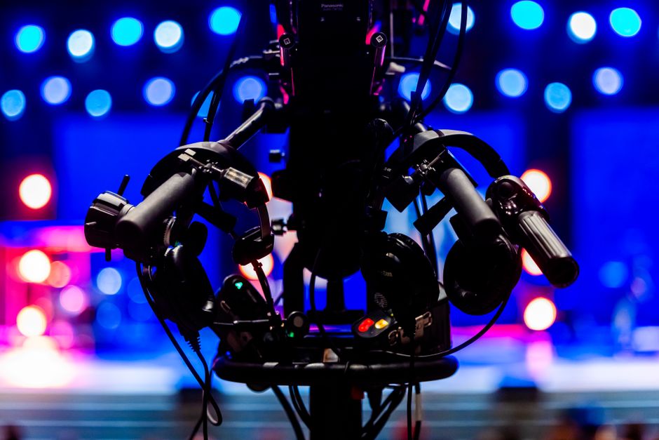 Silhouette of a professional video camera with colorful stage lights in the background.