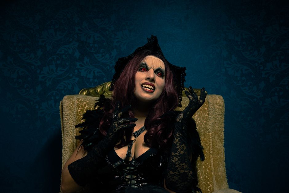 A dramatic portrait of a woman in vampire costume with gothic makeup and attire.