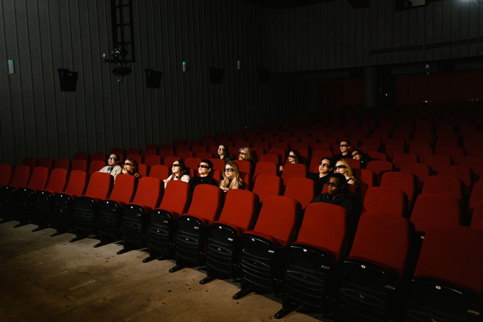 Small group of people wearing 3D glasses watching a movie in a theater with red seats.