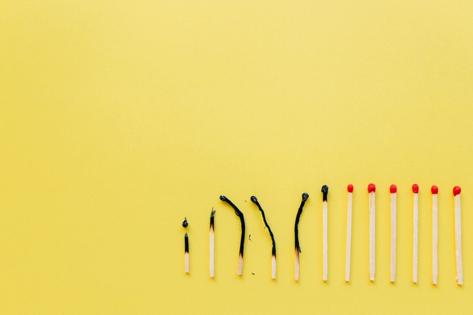 A row of burnt and unburnt matchsticks on a vibrant yellow background illustrating contrast.
