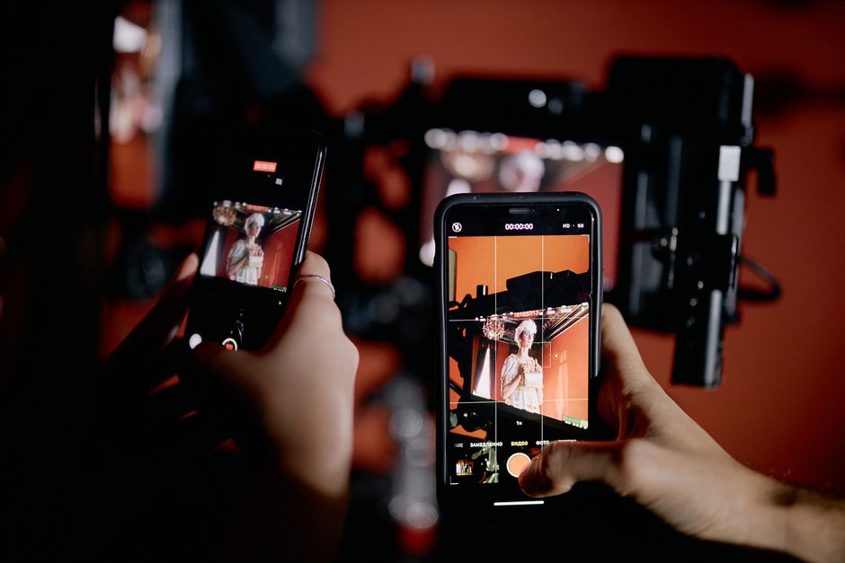 Hands holding smartphones recording a scene indoors with professional equipment.