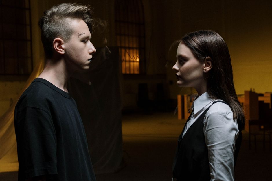 Two young adults facing each other intensely in dim lighting indoors.