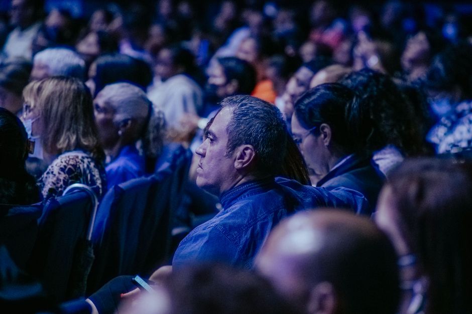 A large, diverse audience attentively listens during an indoor event.