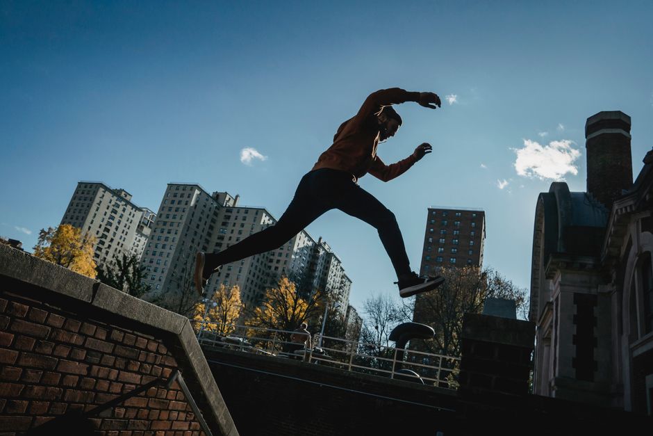 From below full body side view of sportive male performing parkour trick while jumping from railing on street against residential buildings