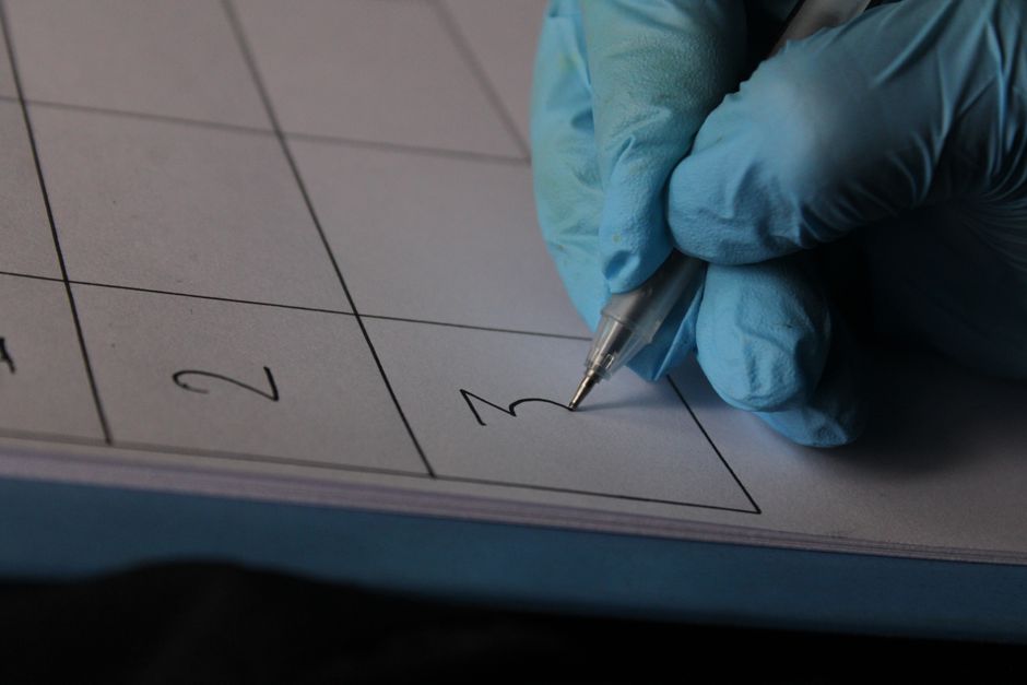 A hand wearing blue gloves writing on a calendar with precision.