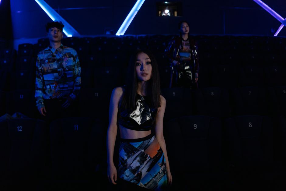 Stylish individuals pose in a dimly lit cinema highlighting vibrant fashion.