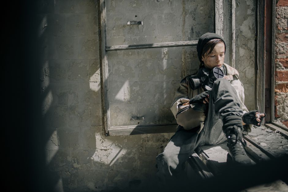A young person in a dilapidated building, wearing a gas mask, reflecting a post-apocalyptic theme.