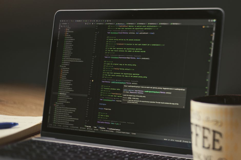 A close-up of a laptop displaying code in a dimly lit room with a coffee mug nearby.