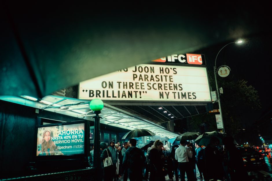 A bustling nighttime crowd under a cinema marquee in New York City.
